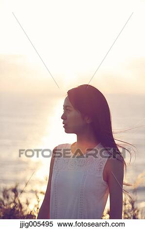 Stock Photography - Young Japanese woman in a white dress at a cliff over the sea at sunrise, Chiba, Japan. Fotosearch