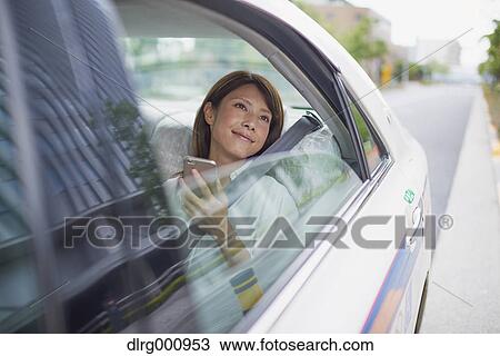 Stock Image - Young Japanese woman riding a taxi downtown Tokyo, Japan. Fotosearch