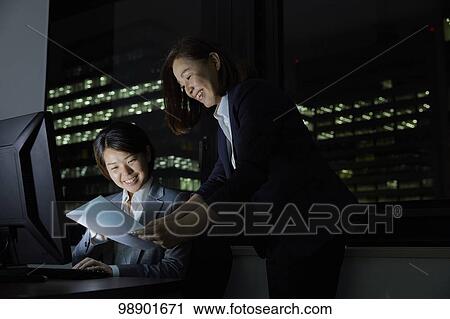 Stock Image - Japanese business people working late at night. Fotosearch