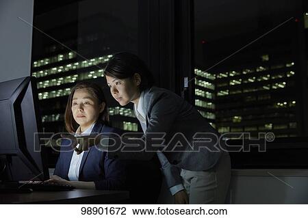 Stock Image - Japanese business people working late at night. Fotosearch