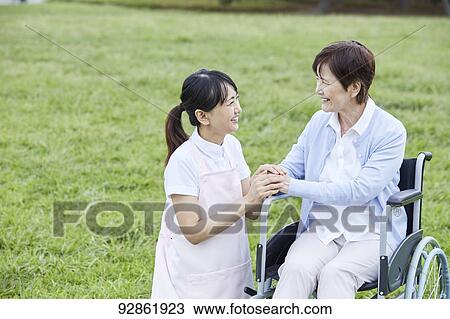 Stock Image - Japanese caretaker helping senior patient. Fotosearch