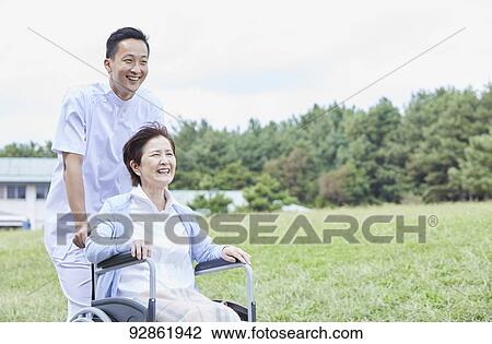 Stock Image - Japanese caretaker helping senior patient. Fotosearch