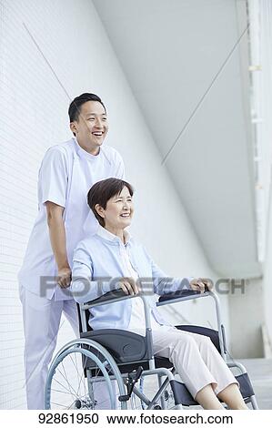Stock Image - Japanese caretaker helping senior patient. Fotosearch