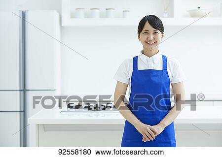 Stock Image - Japanese woman wearing apron at home. Fotosearch