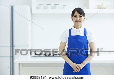 Stock Image - Japanese woman wearing apron at home. Fotosearch