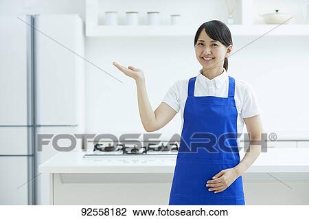Stock Image - Japanese woman wearing apron at home. Fotosearch