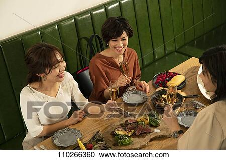 Stock Image - Japanese women happily dining together. Fotosearch