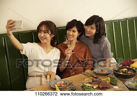 Stock Image - Japanese women happily dining together. Fotosearch