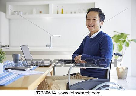 Picture - Japanese young man on wheelchair working from home. Fotosearch
