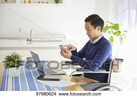 Picture - Japanese young man on wheelchair working from home. Fotosearch