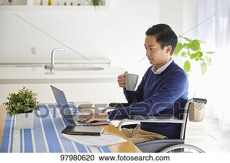 Stock Image - Japanese young man on wheelchair working from home. Fotosearch