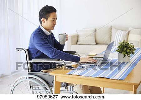 Stock Photo - Japanese young man on wheelchair working from home. Fotosearch