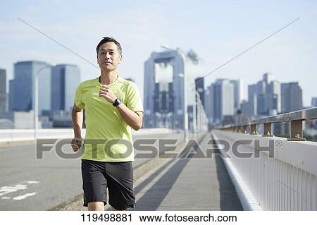 Stock Image - Mature Japanese man running downtown Osaka, Japan. Fotosearch
