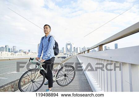 Picture - Mature Japanese man with bike downtown Osaka, Japan. Fotosearch