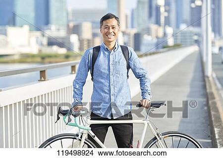Picture - Mature Japanese man with bike downtown Osaka, Japan. Fotosearch