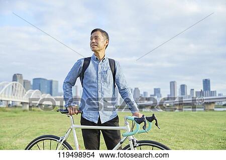 Picture - Mature Japanese man with bike downtown Osaka, Japan. Fotosearch