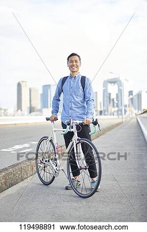 Stock Image - Mature Japanese man with bike downtown Osaka, Japan. Fotosearch