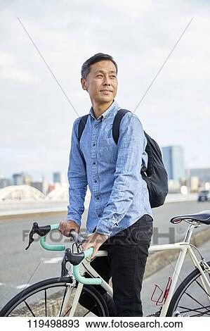 Stock Image - Mature Japanese man with bike downtown Osaka, Japan. Fotosearch