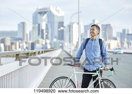 Stock Image - Mature Japanese man with bike downtown Osaka, Japan. Fotosearch