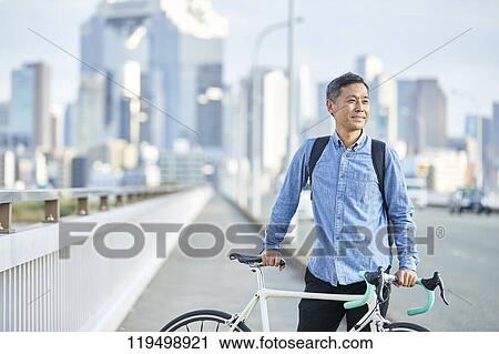Stock Image - Mature Japanese man with bike downtown Osaka, Japan. Fotosearch