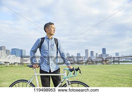 Stock Image - Mature Japanese man with bike downtown Osaka, Japan. Fotosearch