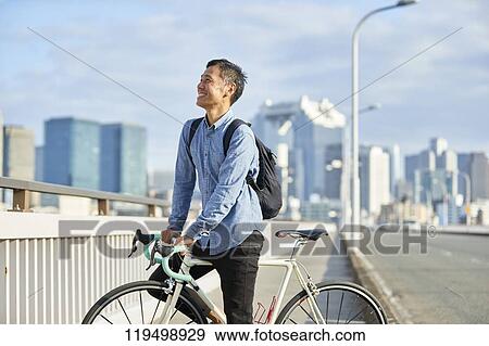 Stock Photo - Mature Japanese man with bike downtown Osaka, Japan. Fotosearch