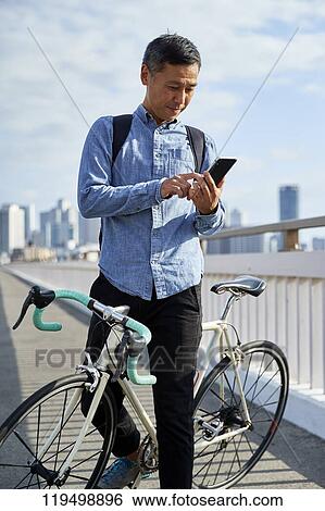 Stock Photograph - Mature Japanese man with bike downtown Osaka, Japan. Fotosearch
