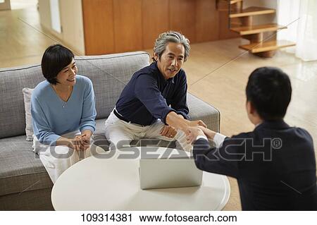 Stock Image - Senior Japanese couple at home with salesman. Fotosearch
