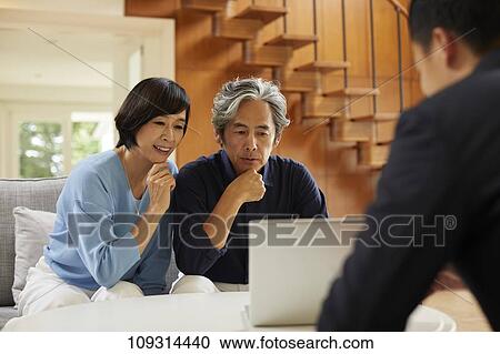 Stock Image - Senior Japanese couple at home with salesman. Fotosearch