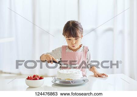 Stock Image - Young happy girl preparing a cake in the kitchen. Fotosearch