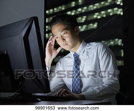 Stock Image - Young Japanese businessman working late at night. Fotosearch