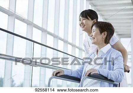 Picture - Young Japanese caregiver taking care of elder patient. Fotosearch