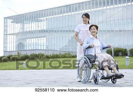 Stock Image - Young Japanese caregiver taking care of elder patient. Fotosearch