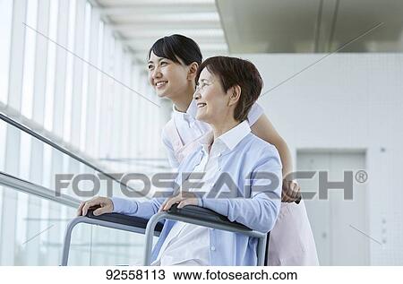 Stock Image - Young Japanese caregiver taking care of elder patient. Fotosearch