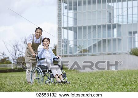 Stock Image - Young Japanese caregiver taking care of elder patient. Fotosearch
