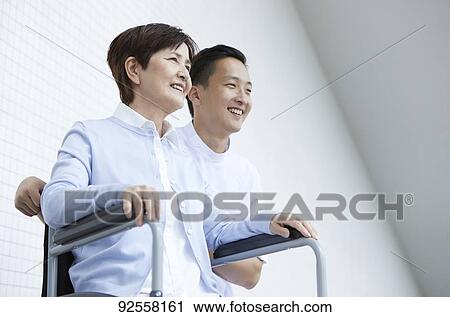 Stock Image - Young Japanese caregiver taking care of elder patient. Fotosearch