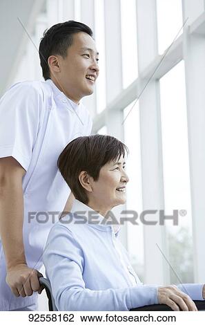 Stock Image - Young Japanese caregiver taking care of elder patient. Fotosearch
