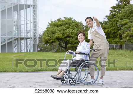 Stock Photo - Young Japanese caregiver taking care of elder patient. Fotosearch