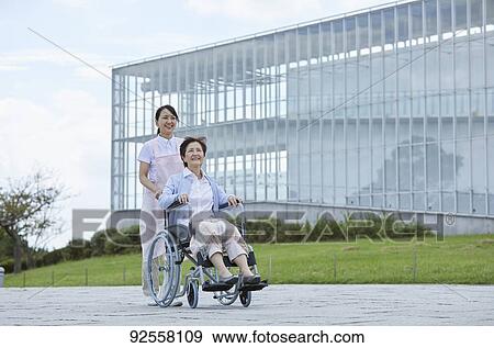 Stock Photo - Young Japanese caregiver taking care of elder patient. Fotosearch