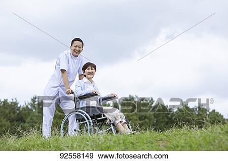 Stock Photo - Young Japanese caregiver taking care of elder patient. Fotosearch