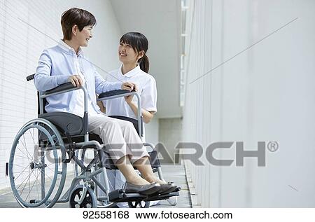 Stock Photo - Young Japanese caregiver taking care of elder patient. Fotosearch
