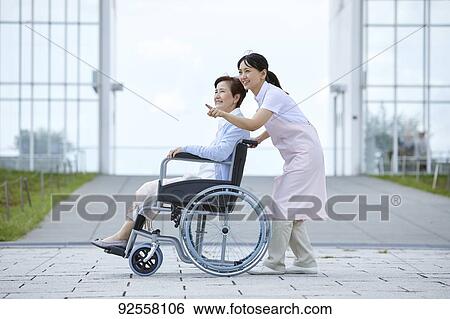 Stock Photograph - Young Japanese caregiver taking care of elder patient. Fotosearch