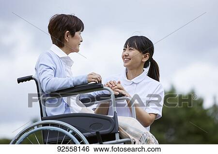 Stock Photograph - Young Japanese caregiver taking care of elder patient. Fotosearch
