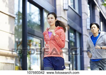 Stock Image - Young Japanese couple running downtown Tokyo. Fotosearch