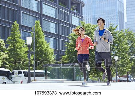 Stock Image - Young Japanese couple running downtown Tokyo. Fotosearch