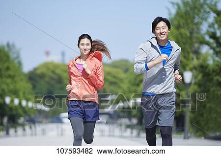 Stock Image - Young Japanese couple running downtown Tokyo. Fotosearch