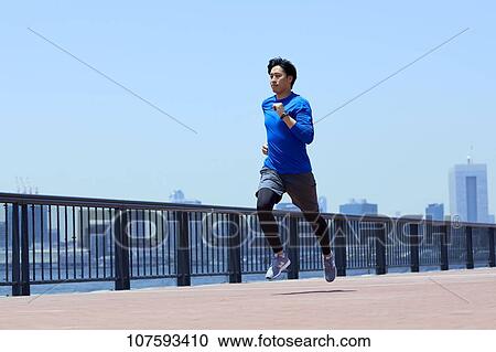 Stock Image - Young Japanese man running downtown Tokyo. Fotosearch