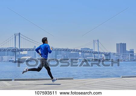 Stock Image - Young Japanese man running downtown Tokyo. Fotosearch
