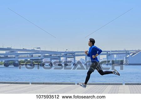 Stock Image - Young Japanese man running downtown Tokyo. Fotosearch