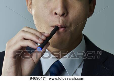 Picture - Young Japanese man smoking electronic cigarette. Fotosearch